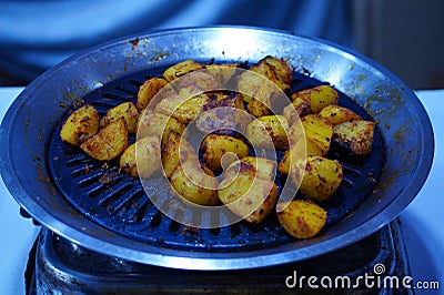 Potato cuts being roasted on a small barbeque machine on a gas stove at night. Stock Photo