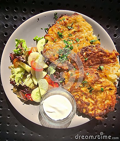 Potato fritters served with sour cream, herbs and salad of fresh seasonal vegetables closeup. Stock Photo