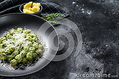 Potato gnocchi with pesto, parmesan cheese and spinach. Italian pasta. Black background. Top view. Copy space Stock Photo