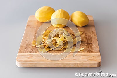 Potato peelings with potatoes on wooden cutting board on grey background Stock Photo