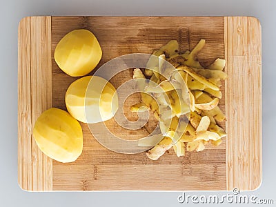 Potato peelings with potatoes on wooden cutting board on grey background. Top view Stock Photo
