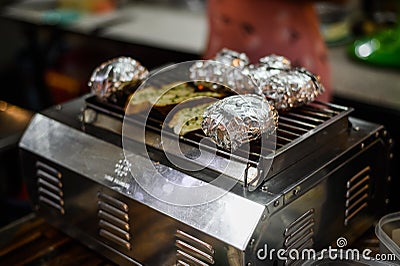 Potatoes in aluminum foil grilling on bbq, summer food Stock Photo