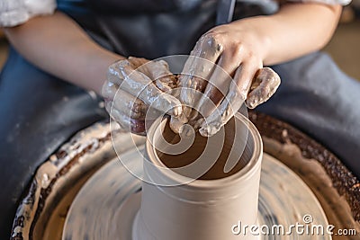 Potter working on a Potter`s wheel making a vase. Woman forming the clay with hands creating jug in a workshop. Close up Stock Photo