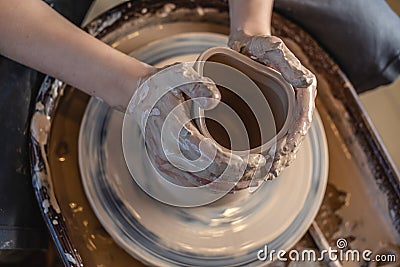 Potter working on a Potter`s wheel making a vase. Woman forming the clay with hands creating jug in a workshop. Top view Stock Photo