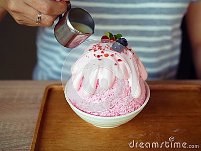 Pour condensed milk over a pink milk kakigori or Japanese shaved ice dessert flavored, topped with pink whipped cream. Stock Photo