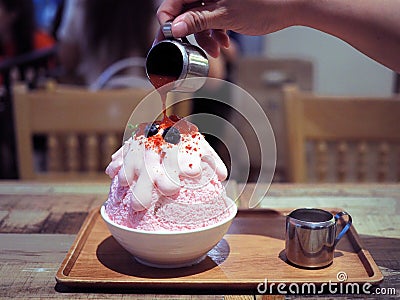 Pour strawberry sauce over a pink milk kakigori or Japanese shaved ice dessert flavored. Stock Photo