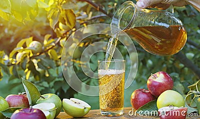 Pouring apple juice into the glass. Fresh organic apples and glass of apple juice on wooden table in the summer orchard garden Stock Photo