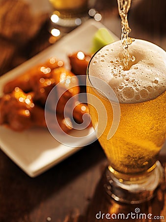 Pouring beer with chicken wings in background. Stock Photo