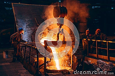 Pouring bright liquid iron or metal with sparks into container in steel mill or workshop blast furnace foundry. Metal Stock Photo