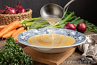 Pouring chicken bone broth from a ladle into a vintage plate Stock Photo