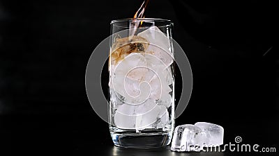 Pouring Cola with ice cubes in glass on black background. Close up. Stock Photo
