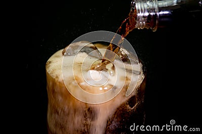 Pouring cola from plastic bottle into rocks glass with ice cubes Stock Photo