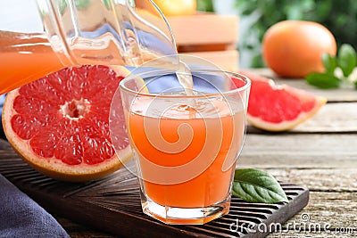Pouring delicious grapefruit juice into glass on wooden table Stock Photo