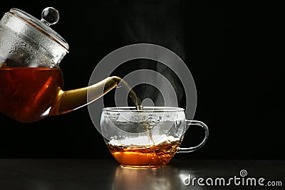 Pouring delicious hot tea into glass cup on table against dark Stock Photo