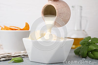 Pouring delicious tofu sauce from saucepan at grey table, closeup Stock Photo