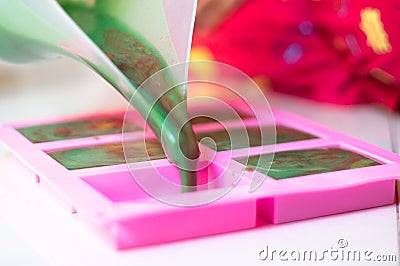 Pouring green colored soap mix with red swirls from a vessle with snout into a pink mold for making final home made hand Stock Photo
