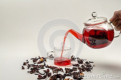 Pouring hibiscus tea from a glass teapot. Scattered dry hibiscus leaves. Stock Photo