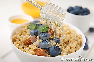 Pouring honey onto delicious cooked quinoa with almonds and blueberries in bowl, closeup Stock Photo