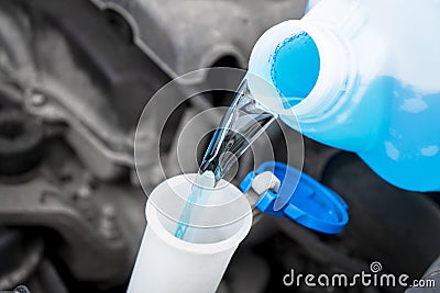 Pouring liquid from plastic canister into car washer fluid reservoir. Close up filling windscreen water tank with washing liquid Stock Photo