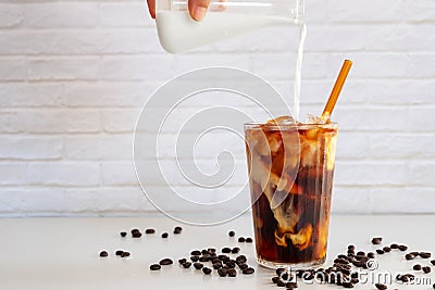 Pouring milk into a glass of homemade cold brew coffee on white Stock Photo