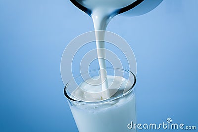 Pouring milk from tin can into a glass on blue background Stock Photo