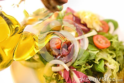 Pouring olive oil from oil dispenser on salad plate Stock Photo