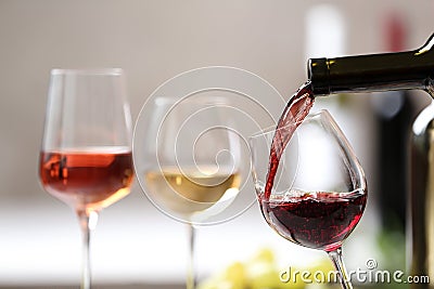 Pouring red wine from bottle into glass on blurred background Stock Photo