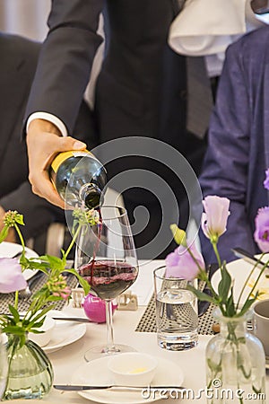 Pouring red wine from bottle into glass at the Party table decorated with beautiful flowers Stock Photo