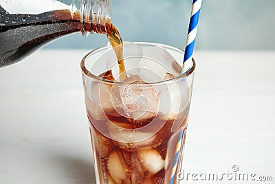 Pouring refreshing soda drink into glass with ice cubes on blurred background Stock Photo