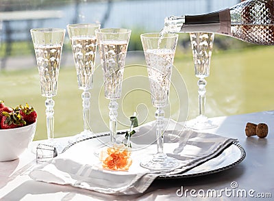 Pouring rose wine into a tall crystal flute glass with other filled glasses in behind, against a bright sunny window. Stock Photo