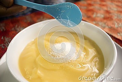 Pouring some sugar in a bowl of yellow pap meal or ogi Stock Photo