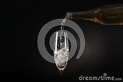 Pouring sparkling wine from bottle into glass on black background Stock Photo