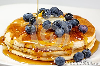 Pouring syrup over the butter on the blueberry stack of pancakes on the kitchen table waiting to be eaten Stock Photo