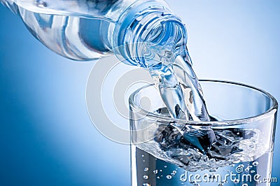 Pouring water from bottle into glass on blue background Stock Photo