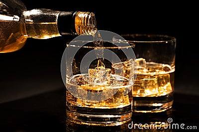 pouring whiskey into a glass from bottle with ice cubes on black Stock Photo