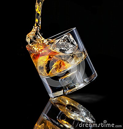 Tilted stylish glass of whiskey. Pouring over cubes ice on black background with reflection Stock Photo