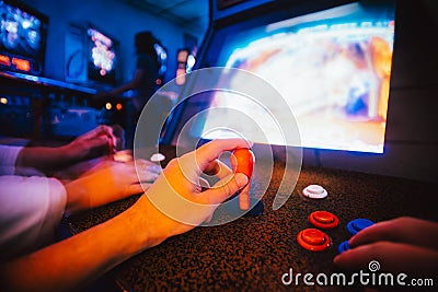 POV angle on hands playing vintage arcade game with an opponent, in a dark shade room full of arcade games Stock Photo
