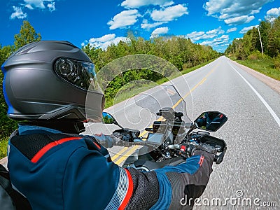 POV side view biker riding motorcycle against blue sky, green trees along the asphalt road. First-person view. Focus on the Stock Photo