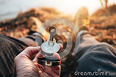 POV view of traveler hold compass in hand and legs in hiking boot. Blurred background Stock Photo