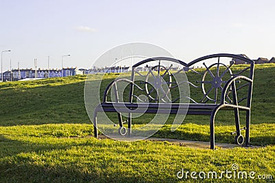A powder coated metal park bench in contemporary design backlit with the soft light of the winter sun Stock Photo