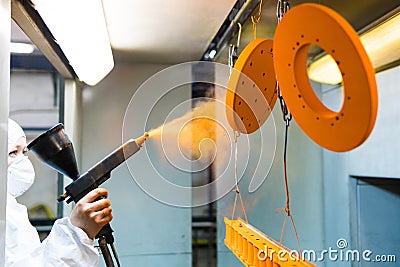 Powder coating of metal parts. A woman in a protective suit sprays powder paint from a gun on metal products Stock Photo