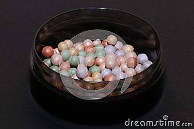 Powder and highlighter with balls of brown, nude, lilac and green colors, isolated on a black background Stock Photo