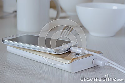 Power bank charges cell phone on the kitchen table Stock Photo