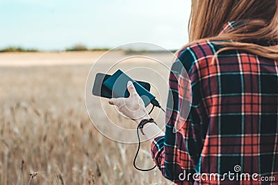 Power Bank in the hand of a girl, against the background of a yellow field. Stock Photo