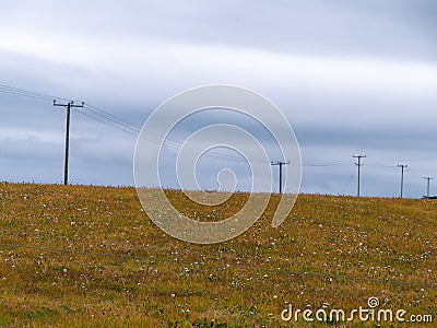 A power lines in a field, sky. Minimalistic landscape, electric post on grass field under white cloudy sky Stock Photo