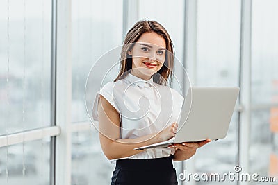 Joyful business woman standin in office, holding laptop. Stock Photo