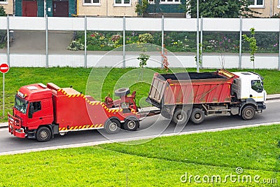 Powerful big red semi evacuation truck tractor tows with attached broken evacuated truck with body driving on city highway Stock Photo