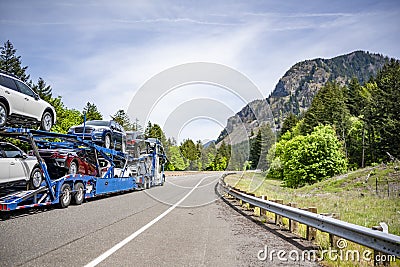 Powerful big rig car hauler semi truck transported cars on the hydraulic modular semi trailer running on the highway road in Stock Photo
