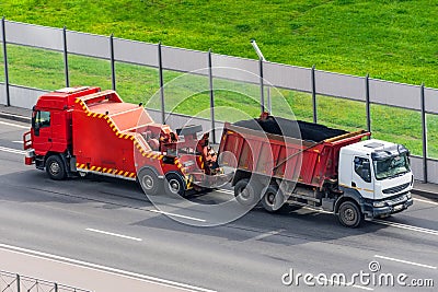 Powerful big rig semi evacuation truck tractor tows with attached broken evacuated truck with body driving on city highway Stock Photo
