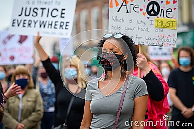 A powerful black female leader wears a Black Lives Matter PPE face mask ahead of other protesters holding signs at a BLM protest Editorial Stock Photo